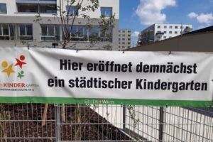 Transparent hängt auf einem Zaun mit dem Text Hier eröffnet demnächst ein städtischer Kindergarten