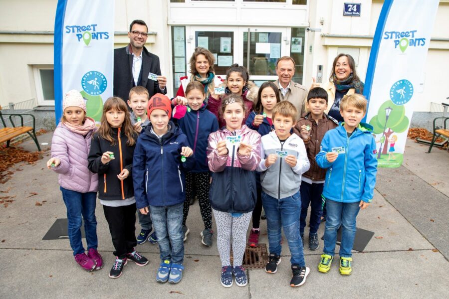 Gruppe von Kindern mit 4 Erwachsenen vor dem Eingang einer Volksschule