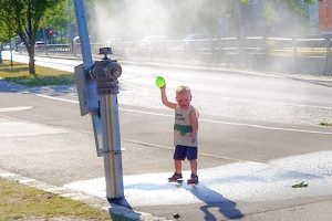Kleinkind steht im Wassernebel einer Sprühnebelanlage