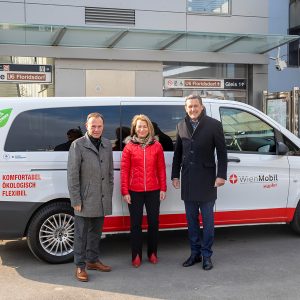 WienMobil Hüpfer Fahrzeug im Hintergrund, im Vordergrund 3 Personen