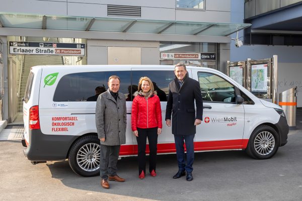 WienMobil Hüpfer Fahrzeug im Hintergrund, im Vordergrund 3 Personen