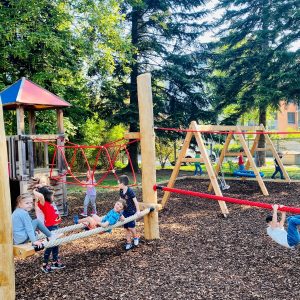 mehrere Kids auf einem Spielgerät, Baume im Hintergrund, Rindenmulch im Vordergrund