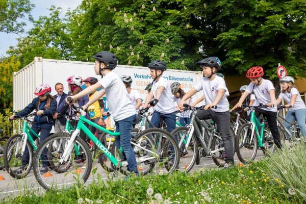 einige Kinder mit Helmen auf Fahrrädern - davor eine grüne Wiese