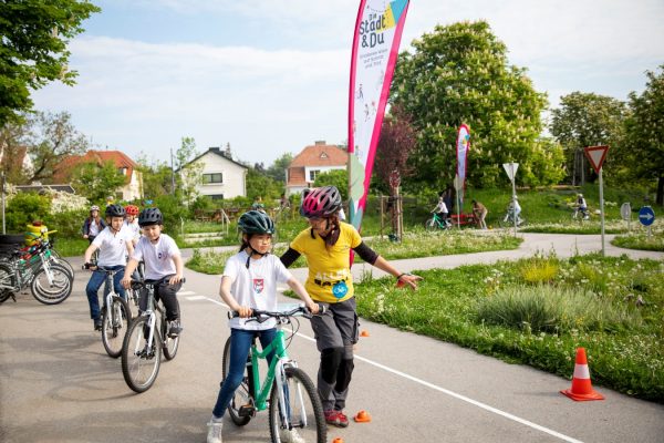 eine Fahrradlehrerin läuft neben einem Fahrrad fahrenden Kind her und sieht zu ihm