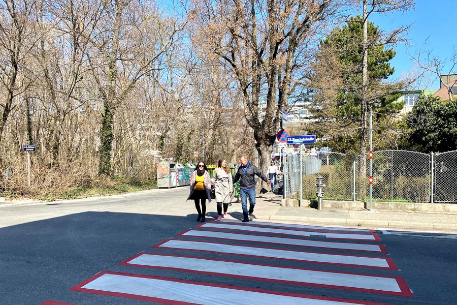 im Vordergrund ein Zebrastreifen, der von drei Personen überquert wird