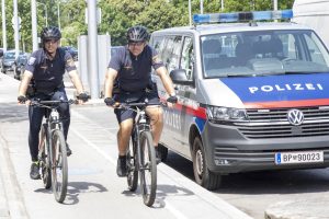 2 radelnde Polizisten auf dem Radweg neben einem geparkten Polizeiauto