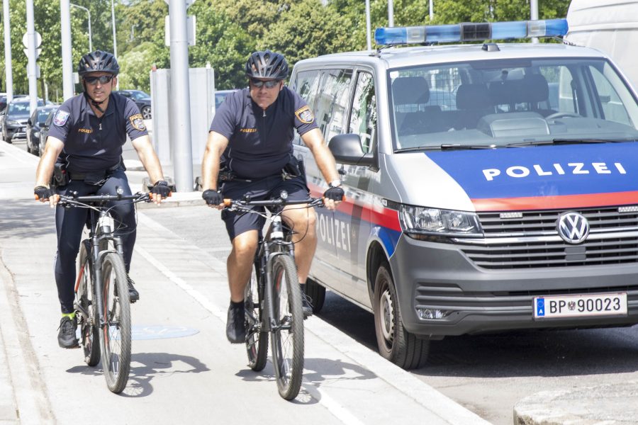 2 radelnde Polizisten auf dem Radweg neben einem geparkten Polizeiauto