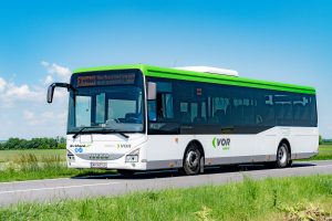 VOR Bus auf einer Straße, Wiese im Vordergrund, blauer Himmel im Hintergrund