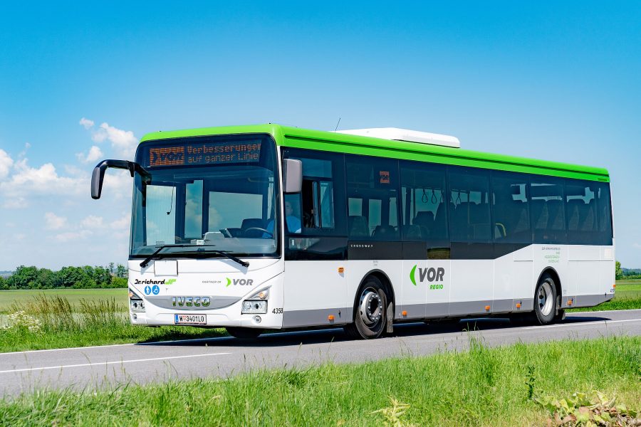 VOR Bus auf einer Straße, Wiese im Vordergrund, blauer Himmel im Hintergrund