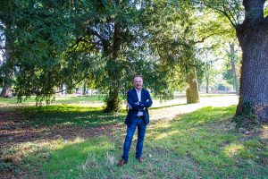 Gerald Bischof steht in der Mitte des Bildes auf einer Wiese, im Hintergrund 2 Bäume