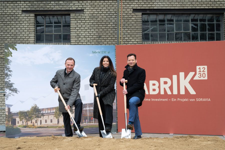3 Personen stehen mit einem Spaten auf einem Sandhaufen, im Hintergrund eine Werbetafel für die Fabrik1230