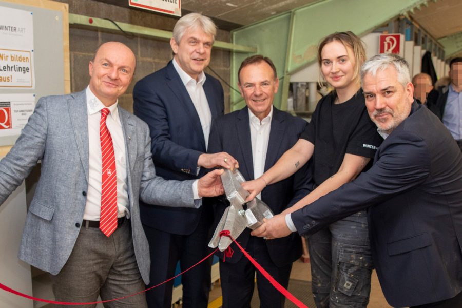 Personen schneiden mit einer überdimensionalen Schere ein rotes Band bei der Eröffnung der Lehrlingsakademie durch. Mit (v.l.n.r.) Ludwig Weichinger-Hieden (Innungsmeister), Matthias Schiffer (WKO), Bezirksvorsteher Gerald Bischof, Lea Decker und Christopher Winter (beide Winter Art),