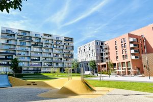 Blauer Himmel, Mehrfamilienhäuser im Hintergrund, Spielplatz im Vordergrund