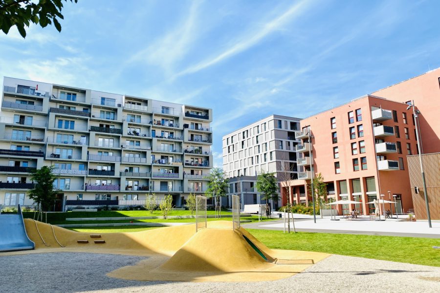 Blauer Himmel, Mehrfamilienhäuser im Hintergrund, Spielplatz im Vordergrund