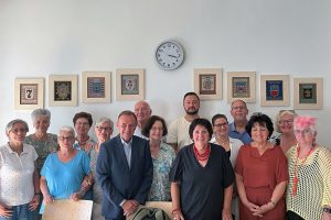 Gruppe von Personen, darüber eine Wanduhr und die Wappen der Liesinger Bezirksteile