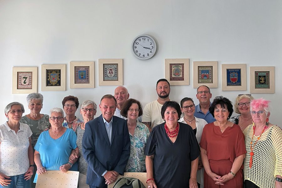 Gruppe von Personen, darüber eine Wanduhr und die Wappen der Liesinger Bezirksteile