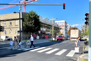 Zebrastreifen, den Personen queren, dahinter Gebäude